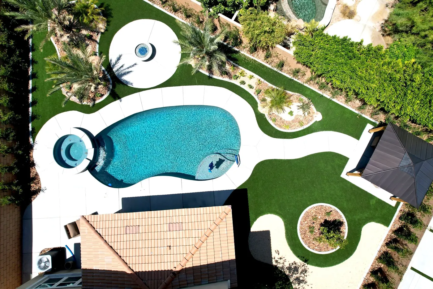 Vista aérea de una piscina de forma libre con césped y un cenador