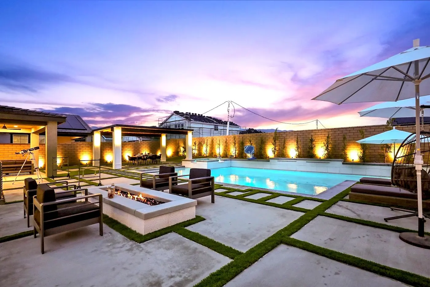 Mesa de fuego, sillones y piscina iluminados al atardecer