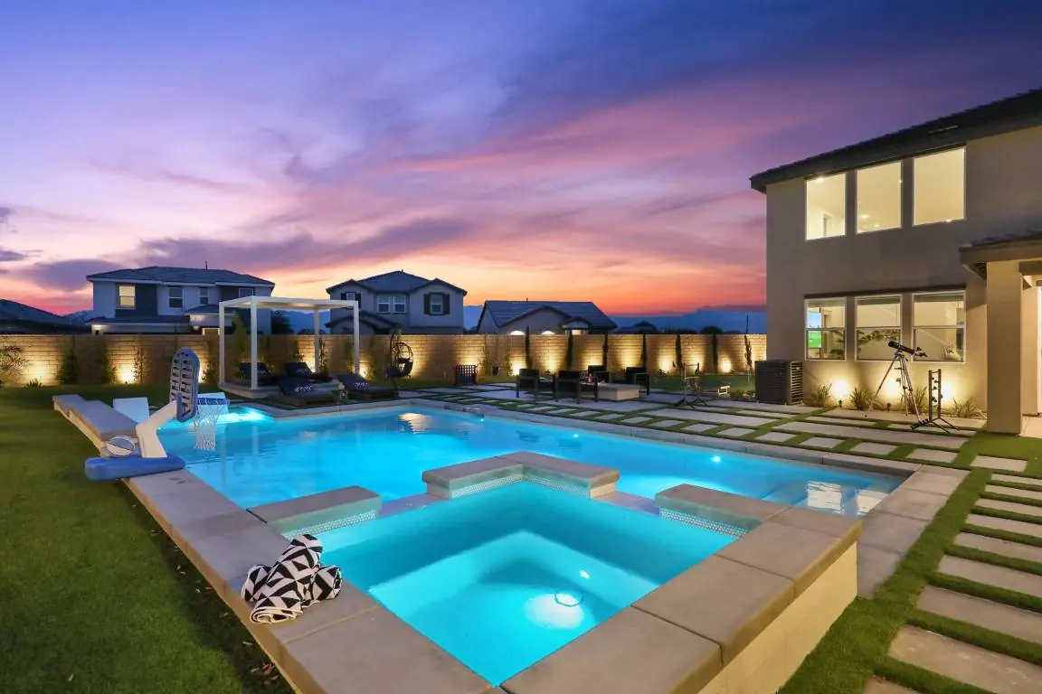 Lit pool with sun shelf and spa under a purple desert sunset