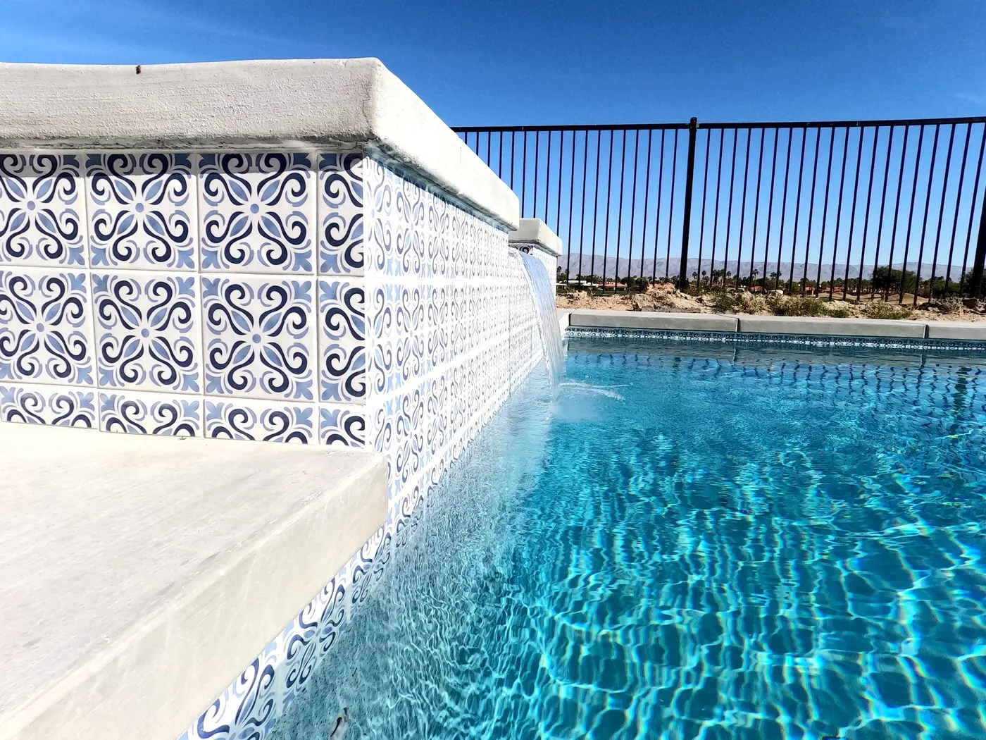 Piscina con un muro de azulejo azul estampado y cascada de lámina de agua