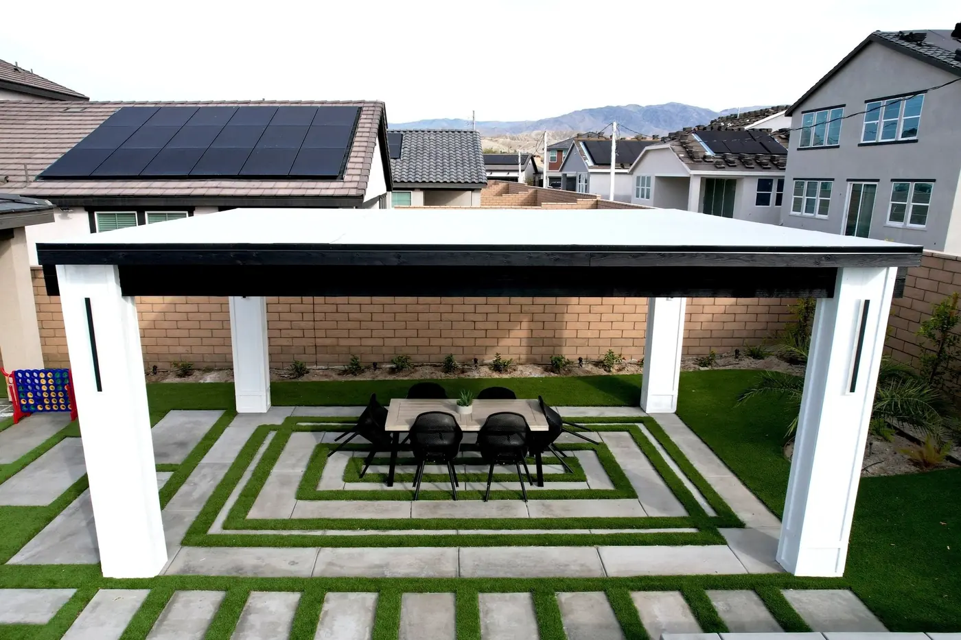White pergola with dining table over turf and pavers